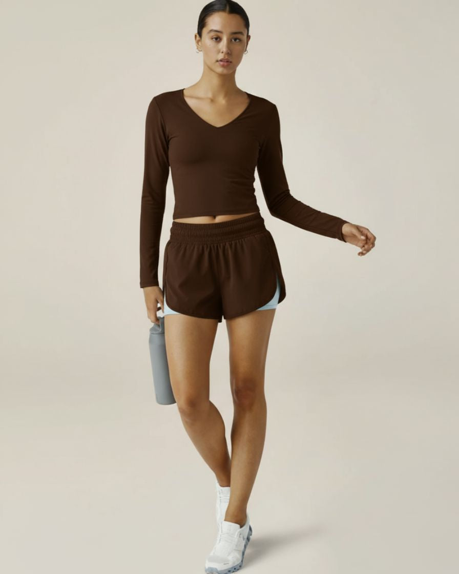 Woman wearing a brown athletic outfit holding a water bottle on a plain background