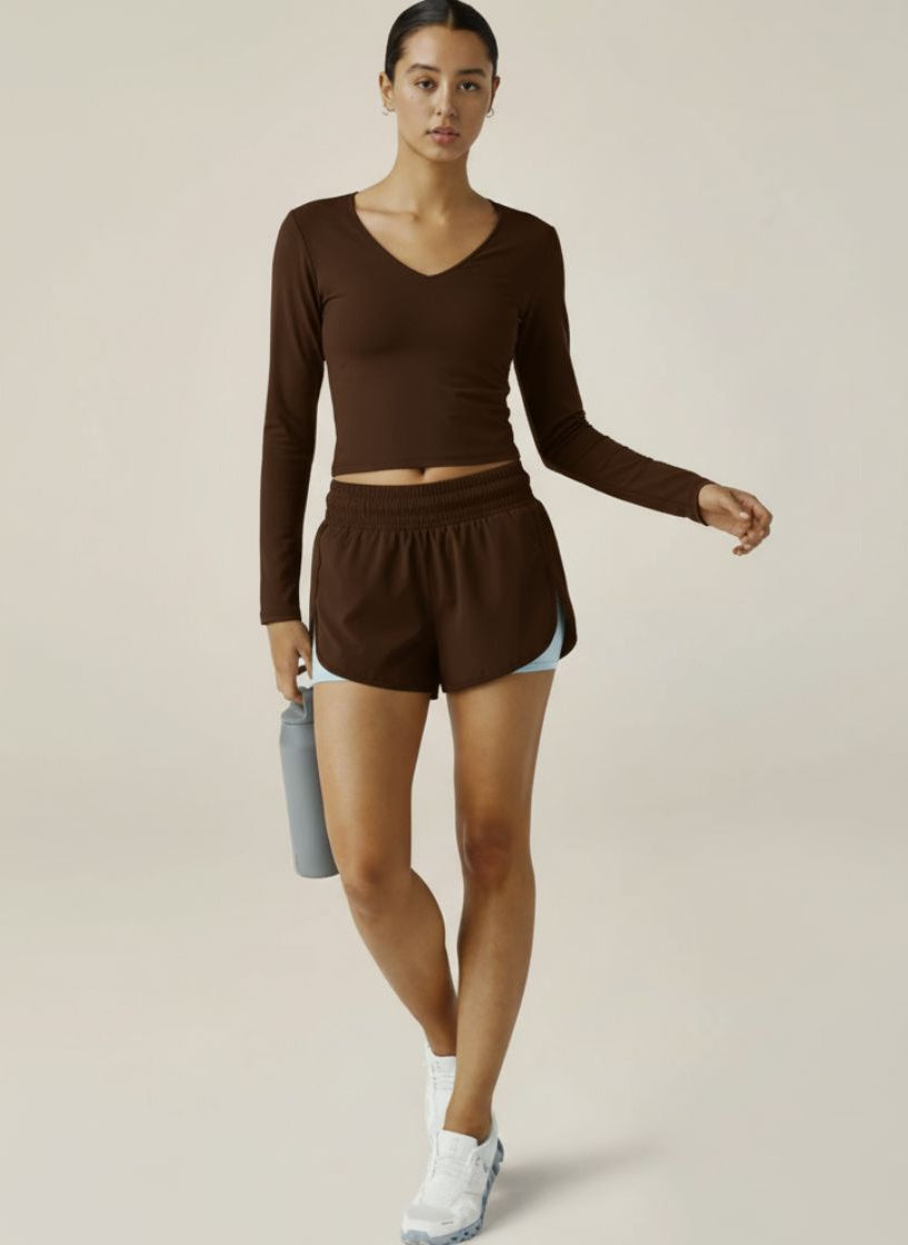 Woman wearing a brown athletic outfit holding a water bottle on a plain background