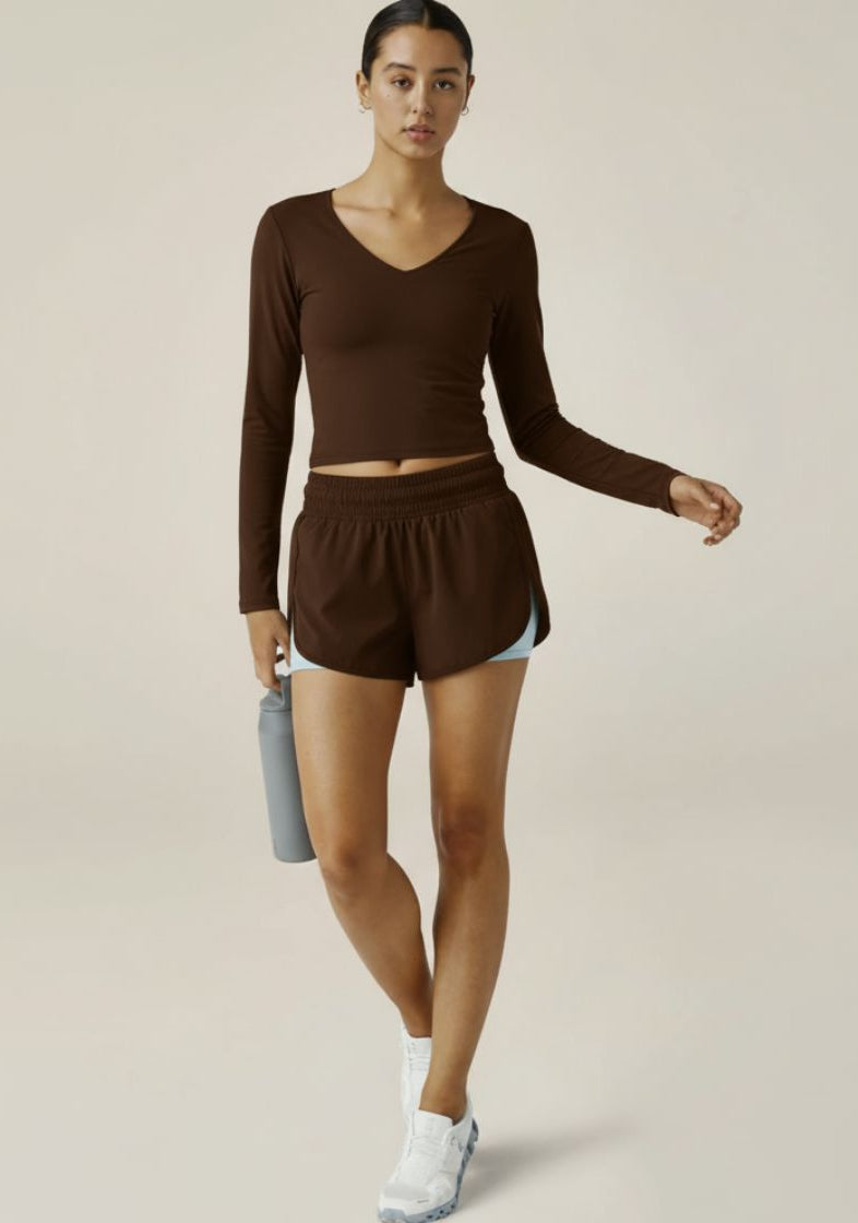 Woman wearing a brown athletic outfit holding a water bottle on a plain background