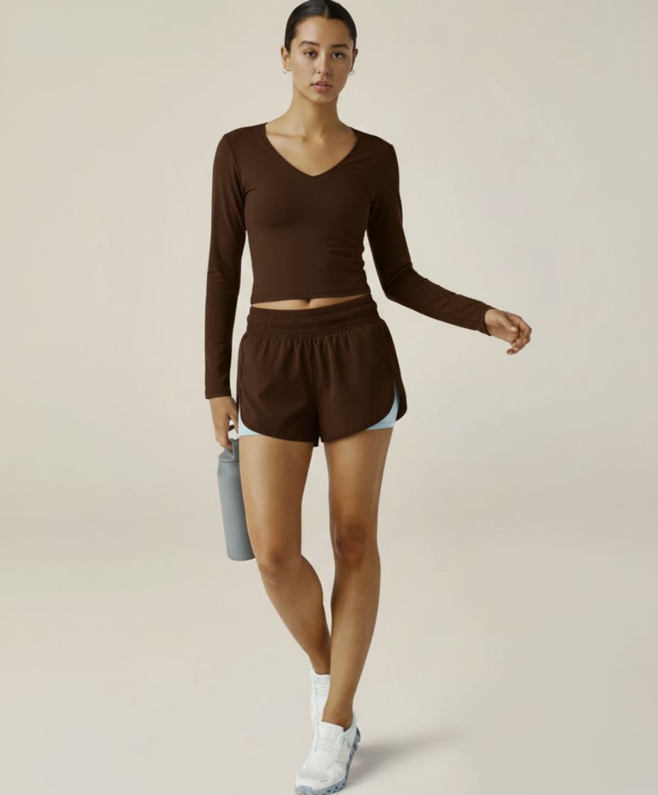 Woman wearing a brown athletic outfit holding a water bottle on a plain background