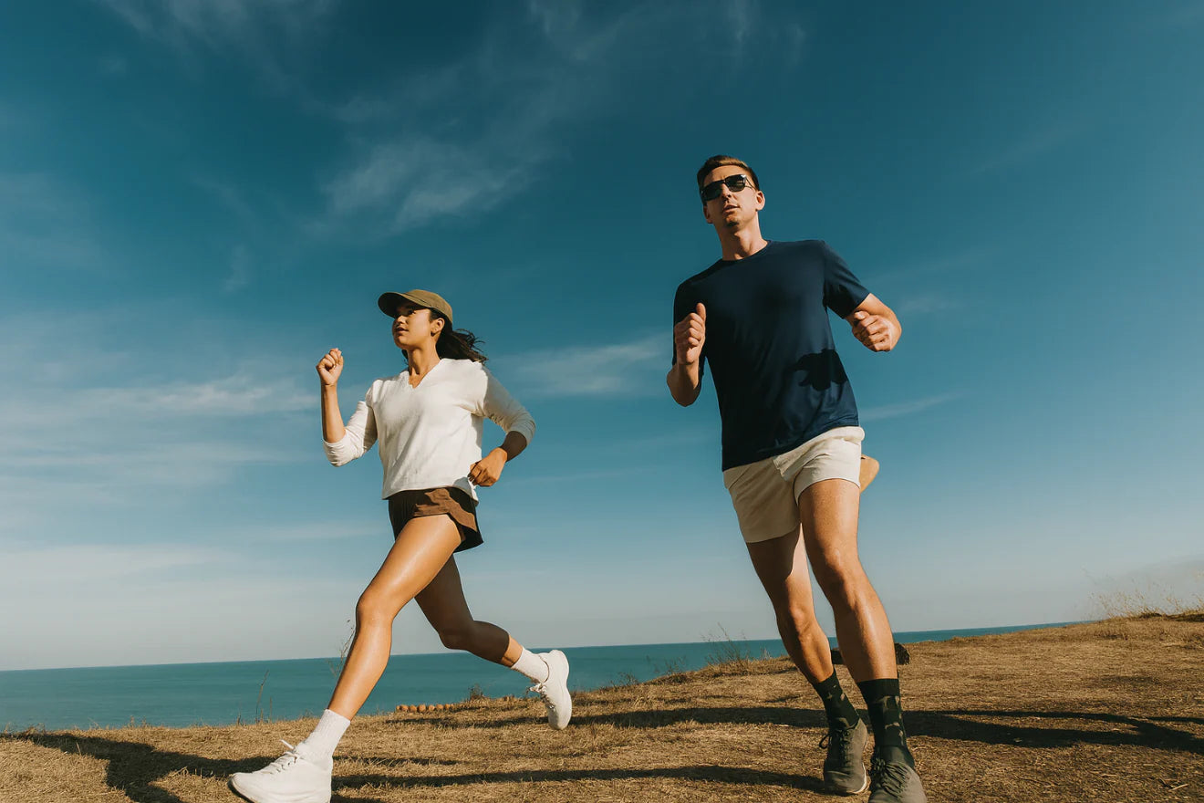 Two people running on a hill wearing terraloop's outfits with a clear blue sky and ocean in the background