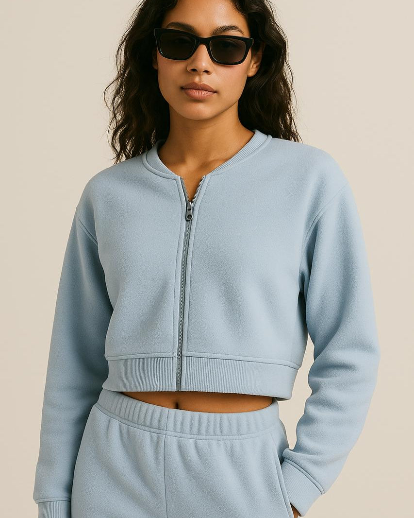 Woman wearing Terraloop's a light blue tracksuit with sunglasses on a beige background