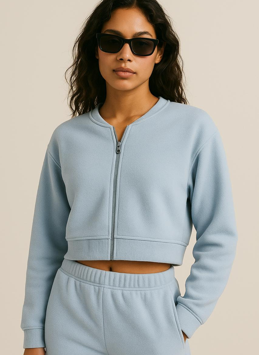 Woman wearing Terraloop's a light blue tracksuit with sunglasses on a beige background