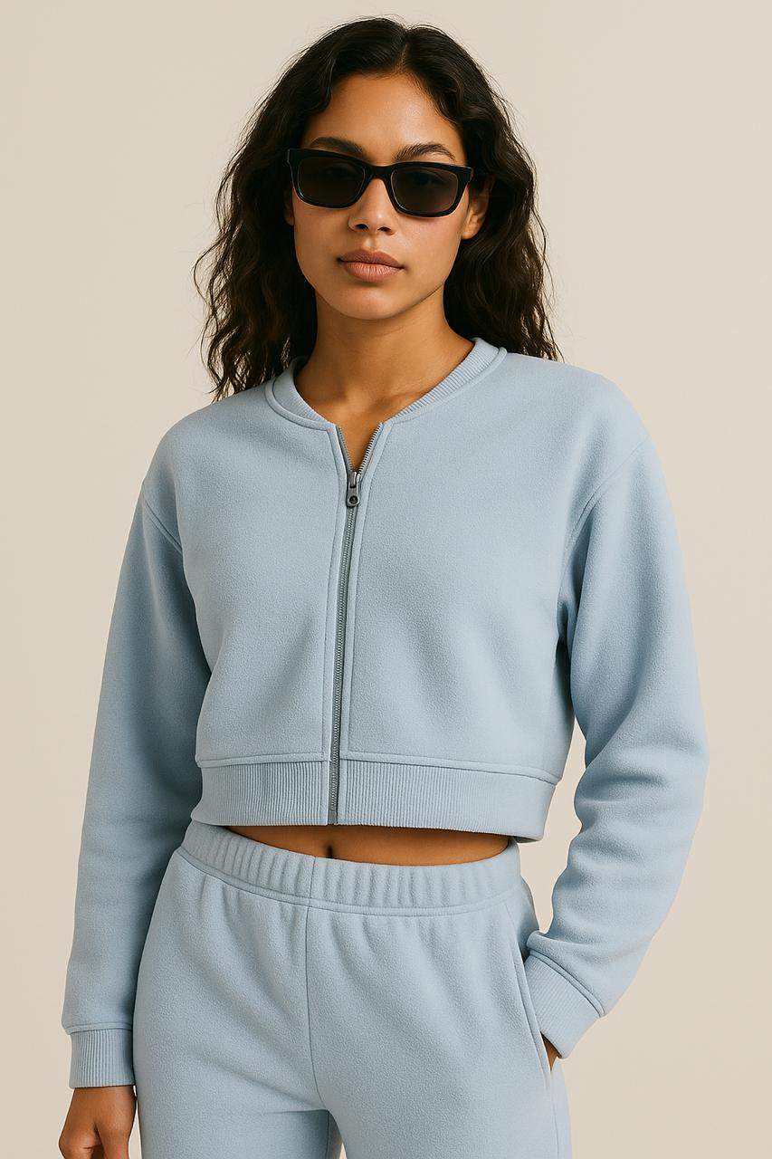 Woman wearing Terraloop's a light blue tracksuit with sunglasses on a beige background